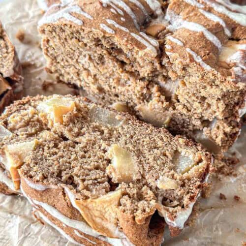 Close-up of sliced apple sourdough bread, topped with a light drizzle of icing. The bread is moist, filled with apple chunks, and rests on parchment paper.