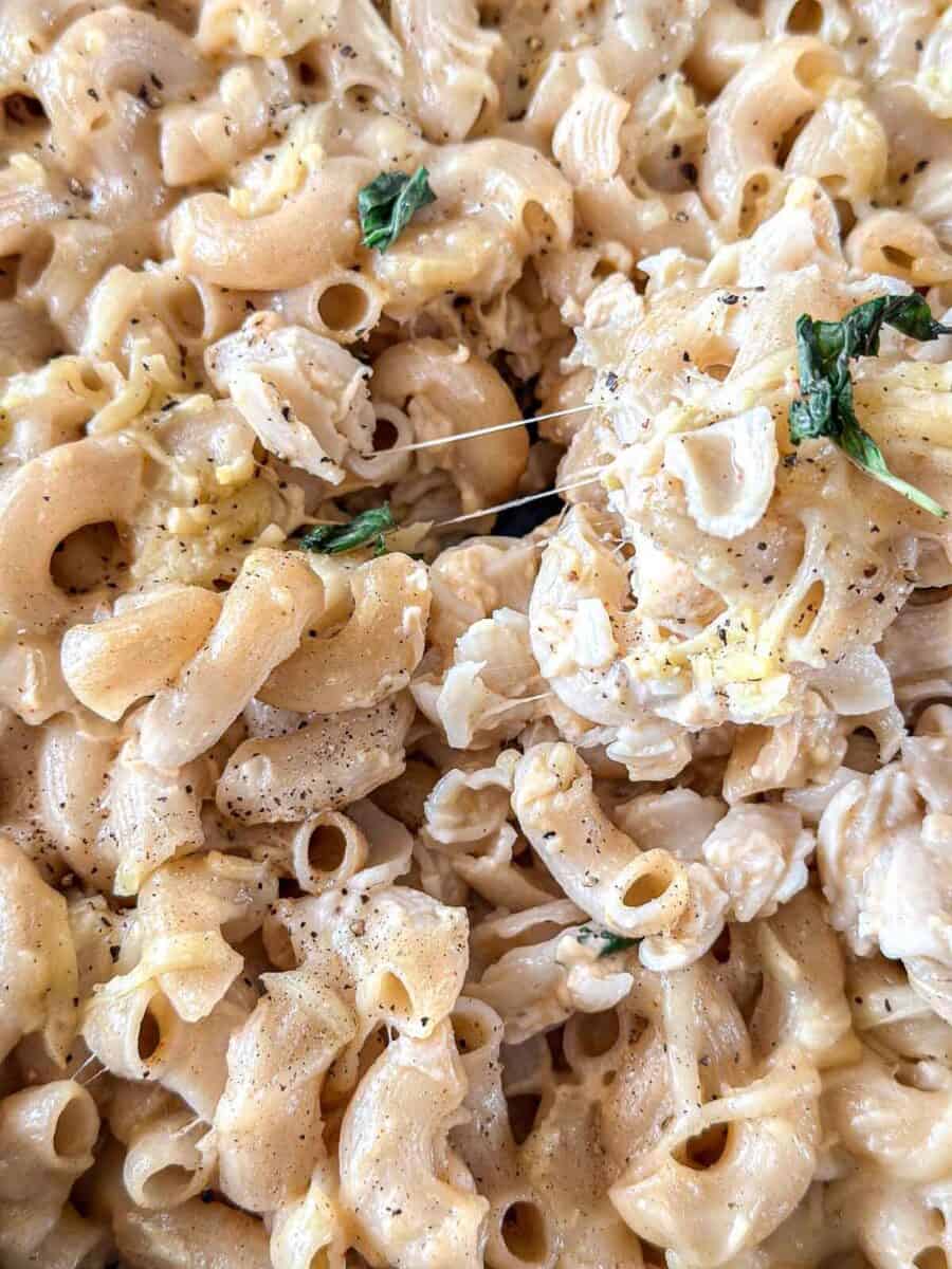 Close-up of creamy smoked macaroni and cheese topped with melted cheese, black pepper, and garnished with fresh green herbs. The pasta appears rich, cheesy, and slightly golden brown.
