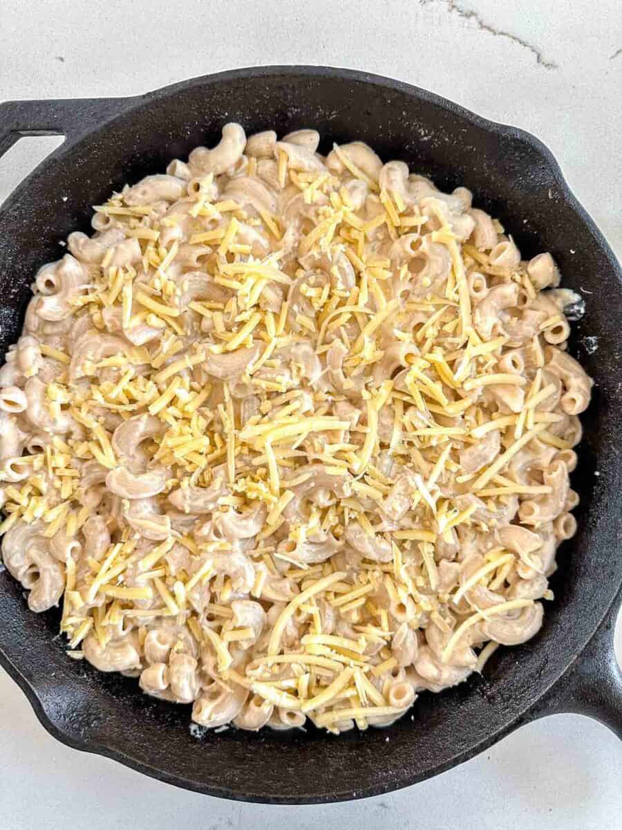 A black cast iron skillet filled with macaroni mixed in a creamy sauce and topped with shredded cheese.