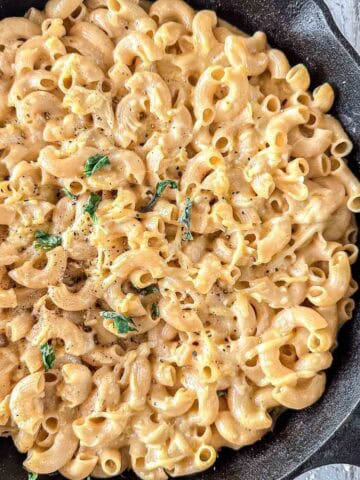 A skillet filled with creamy smoked macaroni and cheese, garnished with fresh basil and a sprinkle of black pepper.