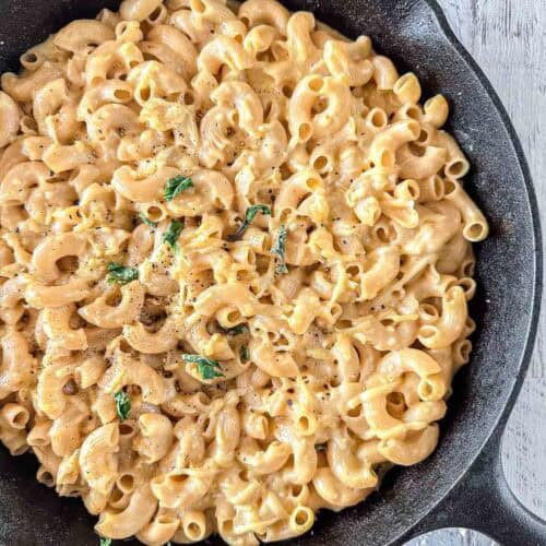 A skillet filled with creamy smoked macaroni and cheese, garnished with fresh basil and a sprinkle of black pepper.