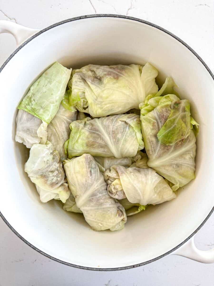 A white pot filled with several stuffed cabbage rolls, tightly wrapped in pale green cabbage leaves and arranged neatly inside.