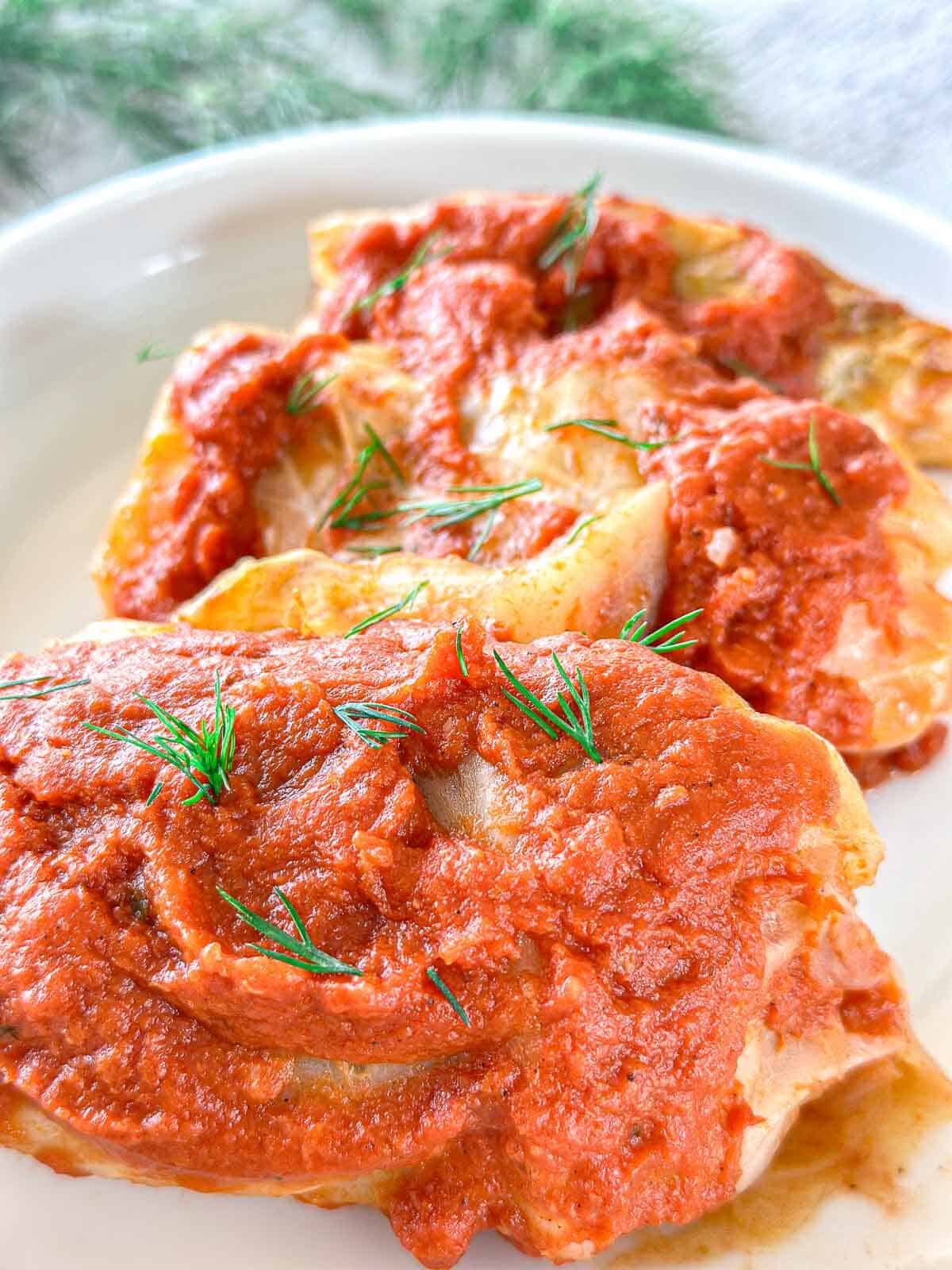 Two cabbage rolls topped with red tomato sauce and garnished with fresh dill, served on a white plate.