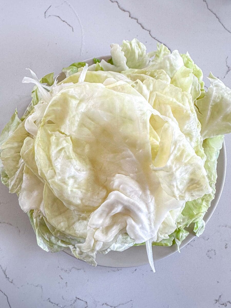 A white plate piled with pale green and white cabbage leaves sits on a light-colored, marbled countertop.