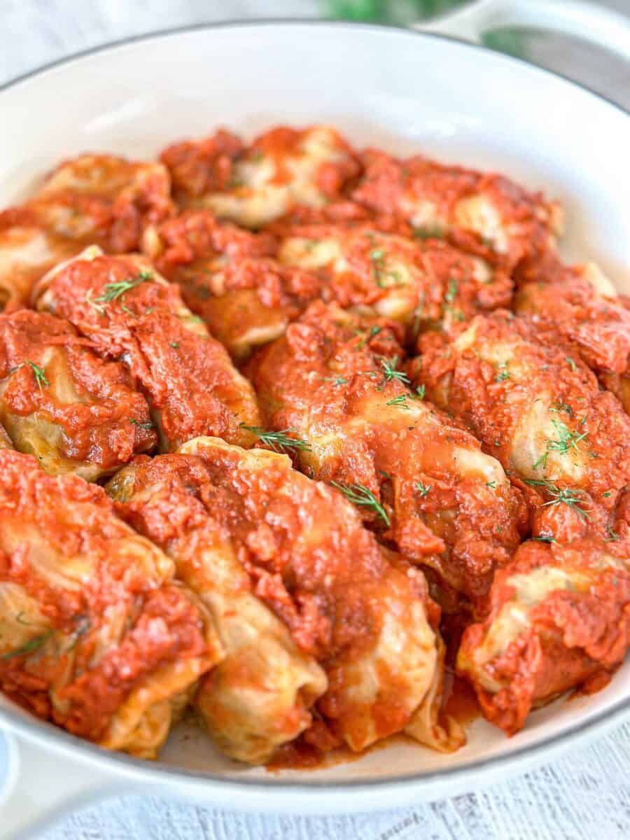 A Dutch oven filled with stuffed cabbage rolls, generously topped with chunky tomato sauce and garnished with fresh herbs.