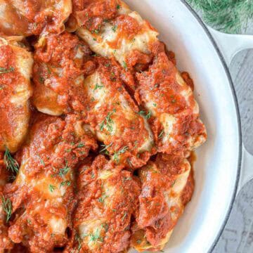 Stuffed cabbage rolls covered in rich tomato sauce, garnished with fresh dill, served in a white Dutch Oven.