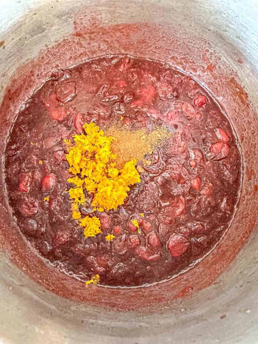 A pot of chunky cranberry sauce with a pile of orange zest and a sprinkle of ground cinnamon on top, ready to be mixed in.
