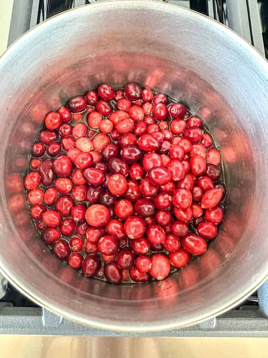 A pot filled with fresh red cranberries simmering on a stovetop, viewed from above.