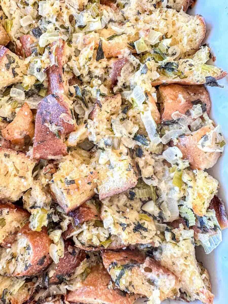 Close-up of homemade bread stuffing with chunks of toasted bread, chopped onions, celery, and herbs, all mixed together and baked until golden brown.