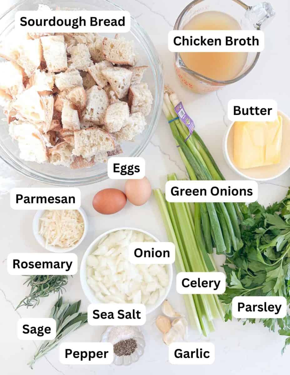 Ingredients for stuffing are laid out and labeled: sourdough bread pieces, chicken broth, butter, eggs, green onions, parsley, celery, onion, garlic, sea salt, pepper, parmesan, rosemary, and sage.