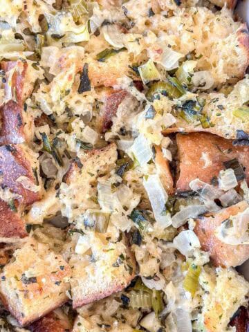 Close-up of homemade bread stuffing with chunks of toasted bread, chopped celery, onions, and herbs, baked until golden and tender in a casserole dish.