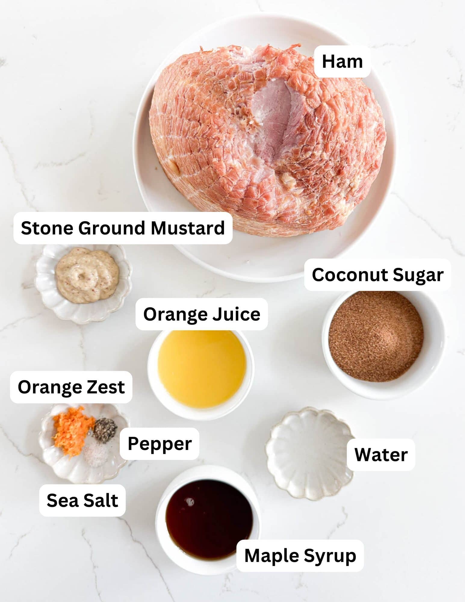 A plate with a ham is surrounded by labeled bowls containing stone ground mustard, coconut sugar, orange juice, orange zest, sea salt, pepper, water, and maple syrup on a white background.
