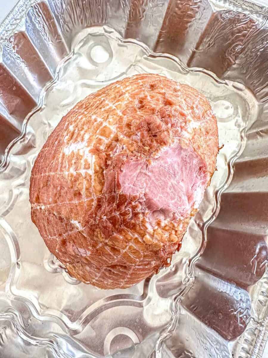 A cooked ham with a crisscross pattern on its surface sits in a disposable aluminum baking pan.