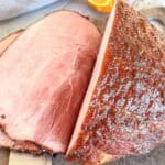 Close-up of a sliced, glazed smoked ham on a cutting board, showing the juicy, pink interior and caramelized, browned outer crust.
