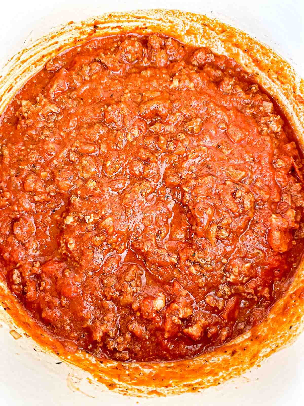 A close-up view of a pot filled with chunky, cooked meat sauce in a rich red tomato base, likely a Bolognese or marinara sauce with ground meat.