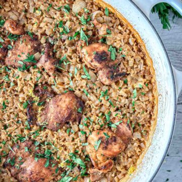Dutch oven chicken and rice featuring seasoned chicken thighs on a bed of golden brown rice, garnished with chopped fresh herbs, in a round white pan.