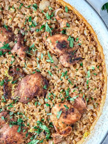 Dutch oven chicken and rice featuring seasoned chicken thighs on a bed of golden brown rice, garnished with chopped fresh herbs, in a round white pan.