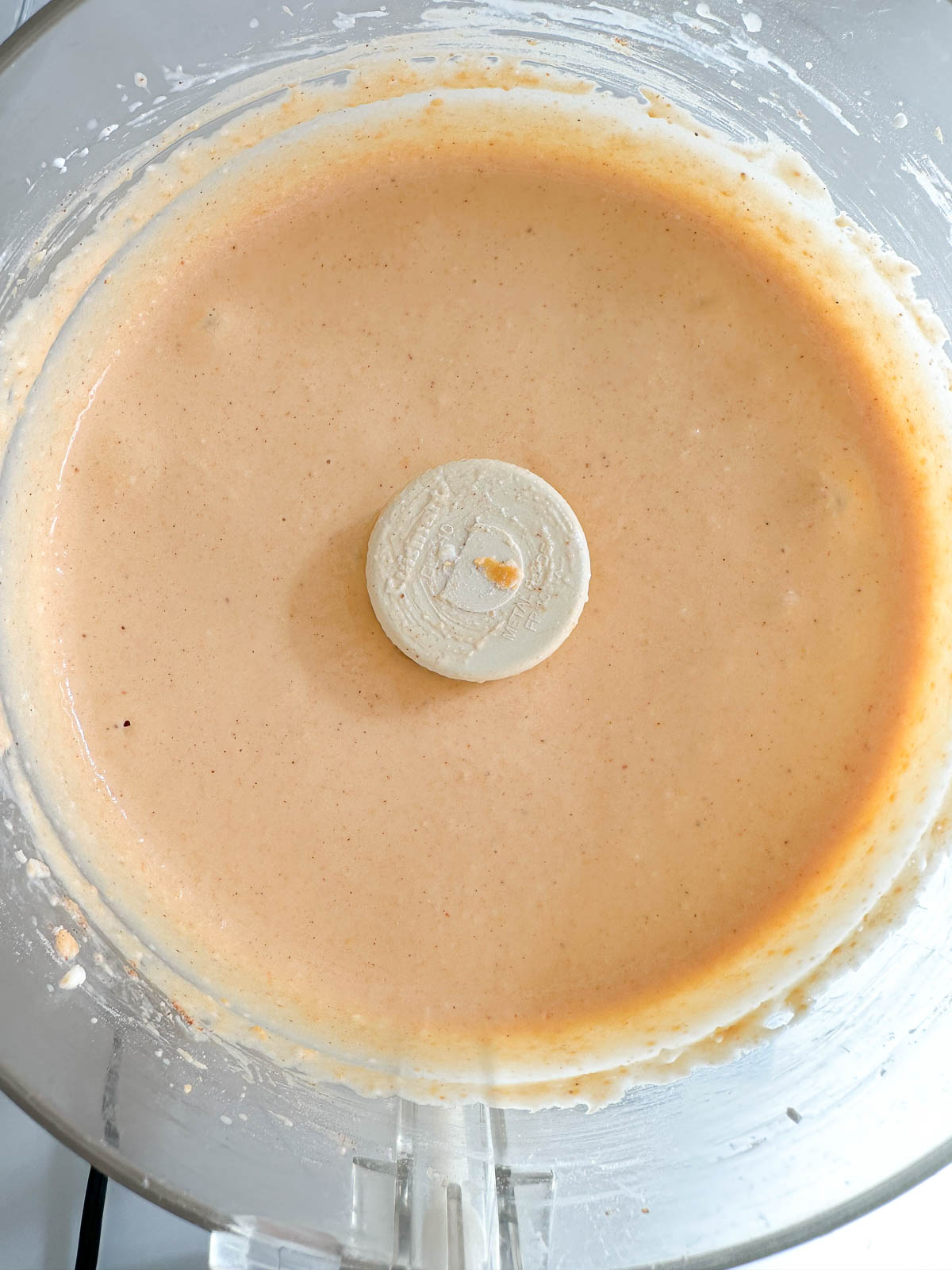 Close-up of a food processor bowl containing a smooth, creamy, light orange mixture with the blade attachment visible in the center.