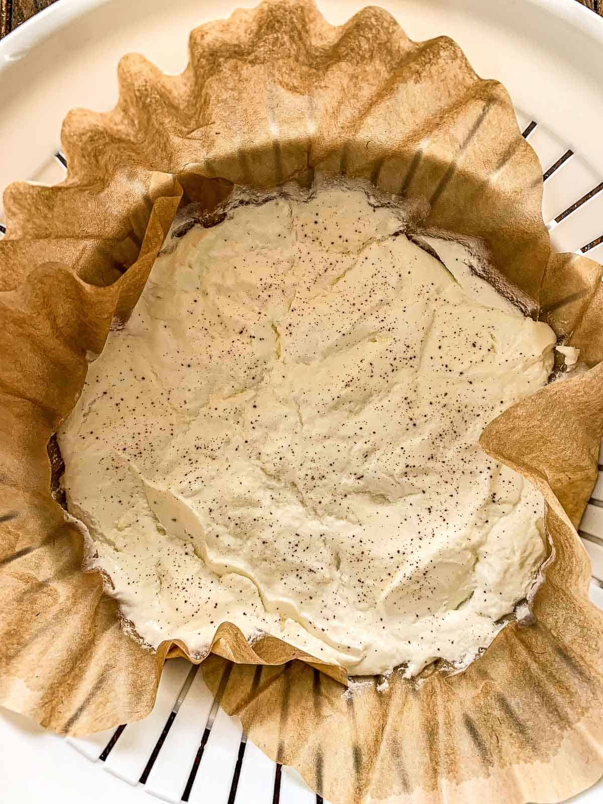A round baking dish lined with crumpled parchment paper, filled with a creamy Turkish Labneh.