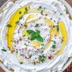 A plate of whipped labneh drizzled with olive oil, sprinkled with chopped herbs and spices, and garnished with a sprig of fresh mint.