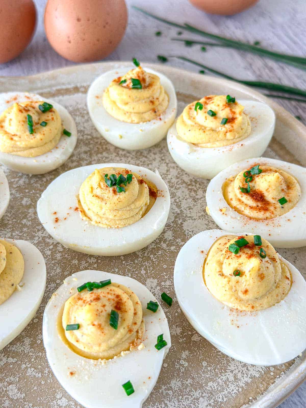 A tray of smoked deviled eggs topped with chopped chives and paprika, with whole eggs and chives in the background.