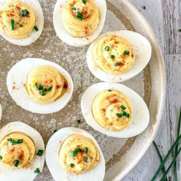 Smoked Deviled eggs arranged on a rustic plate, topped with paprika and chopped chives. The plate sits on a wooden surface, with fresh chives nearby.