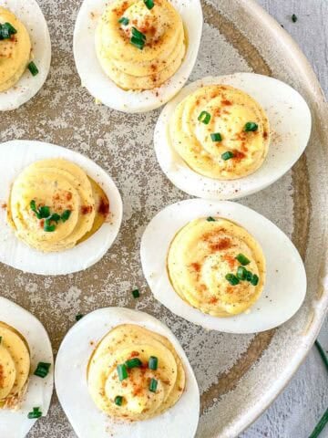 Smoked Deviled eggs arranged on a rustic plate, topped with paprika and chopped chives. The plate sits on a wooden surface, with fresh chives nearby.