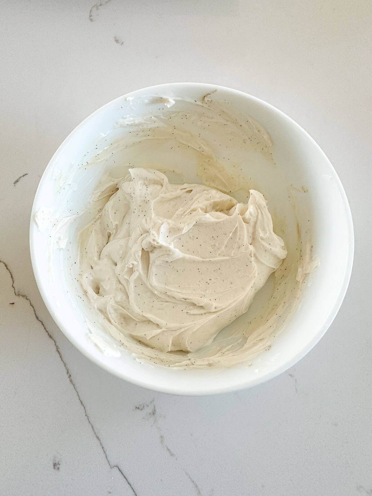 A white bowl filled with creamy labneh frosting speckled with vanilla bean specks.