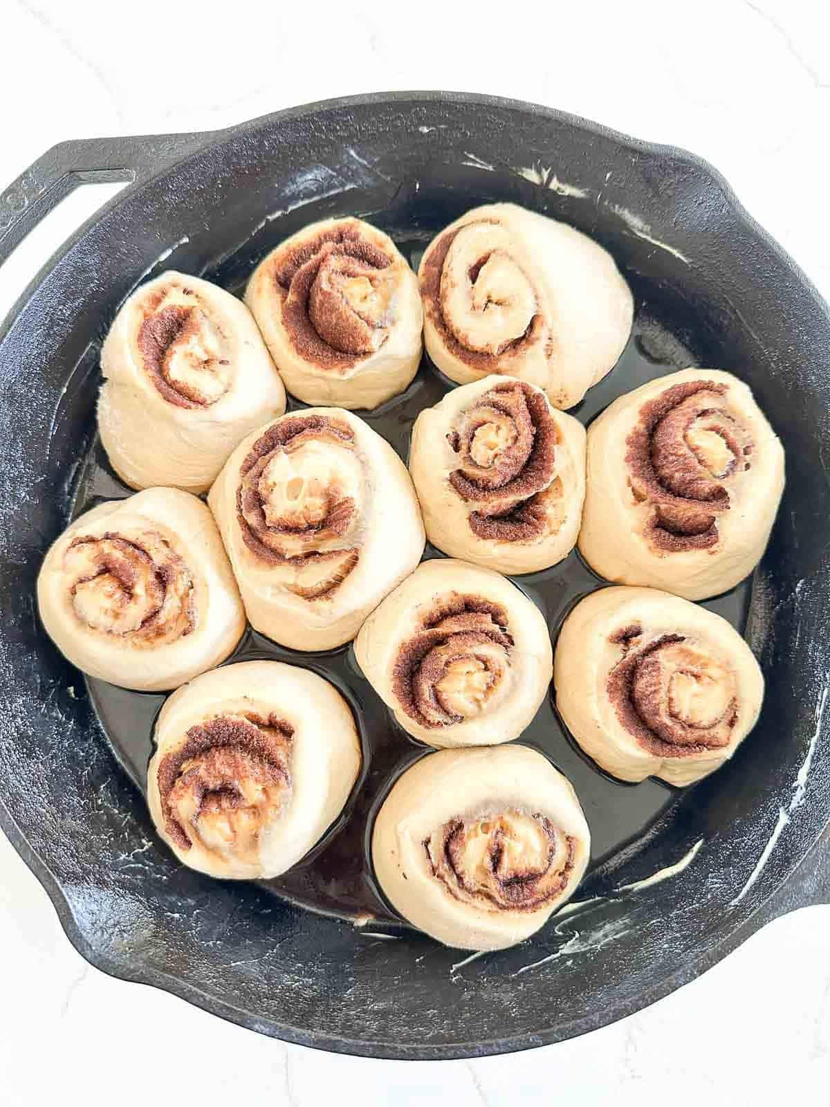 Ten raw cinnamon rolls arranged in a cast-iron skillet.