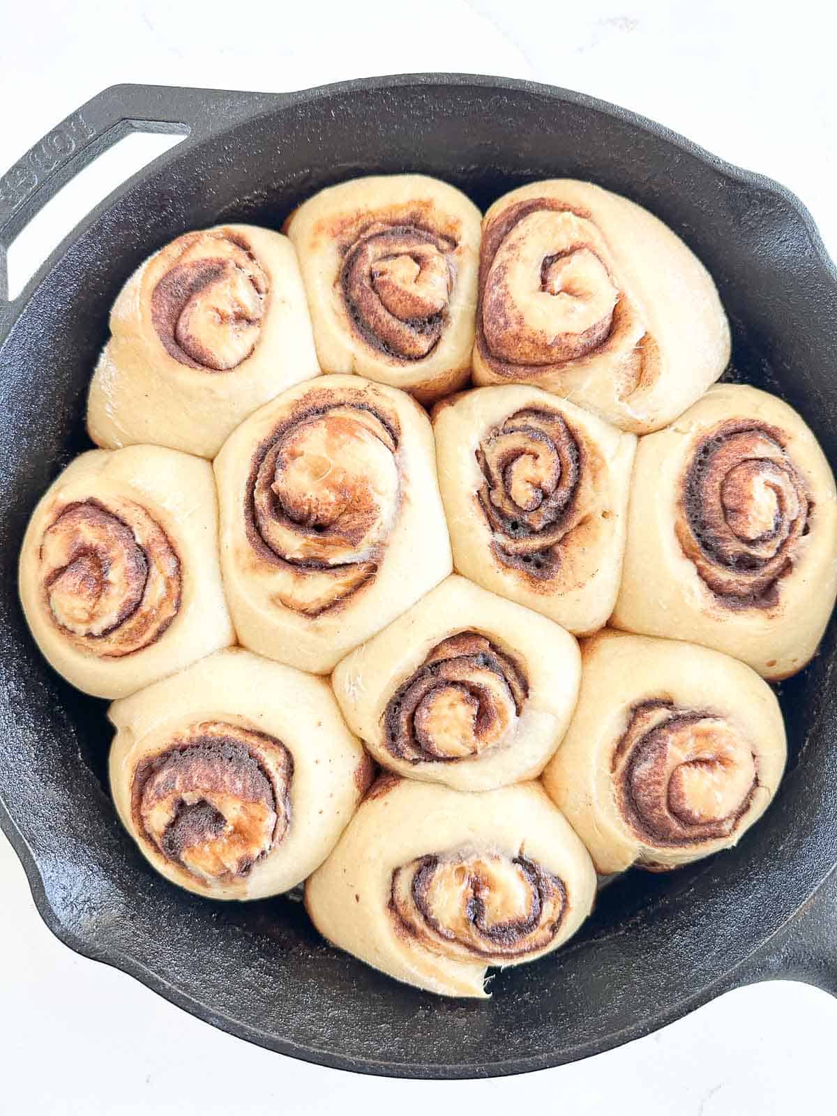 Sourdough cinnamon rolls arranged in a circle inside a black cast-iron skillet.