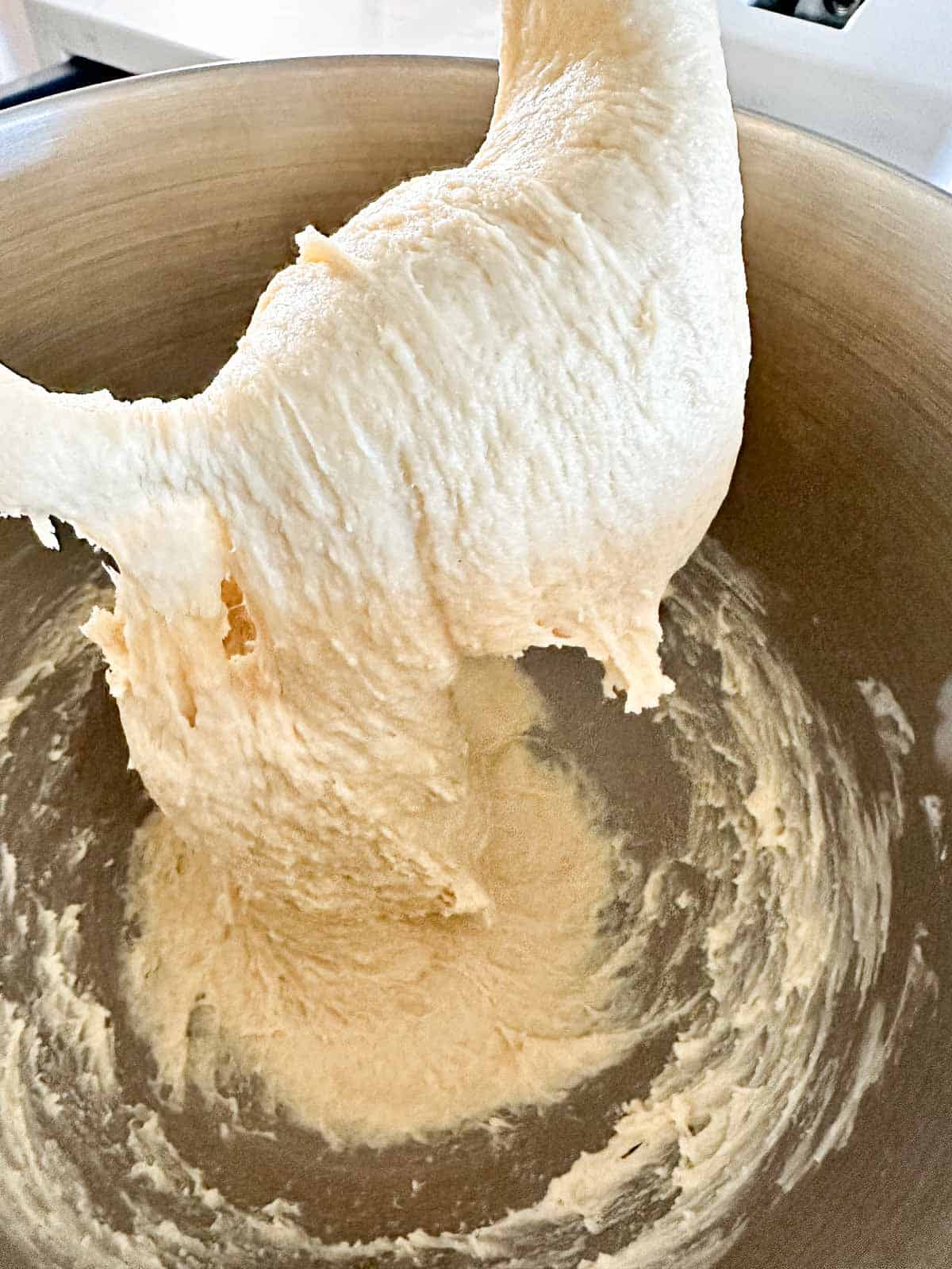 Sticky sourdough dough clinging to a stand mixer hook inside a metal mixing bowl.