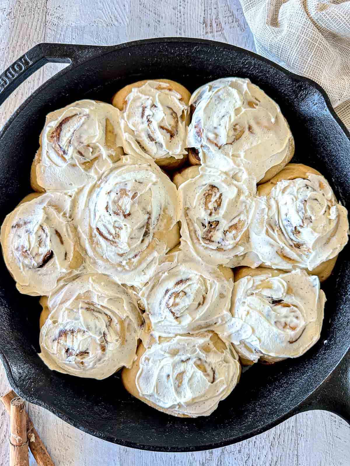 Sourdough cinnamon rolls topped with cream cheese frosting in a black cast iron skillet.