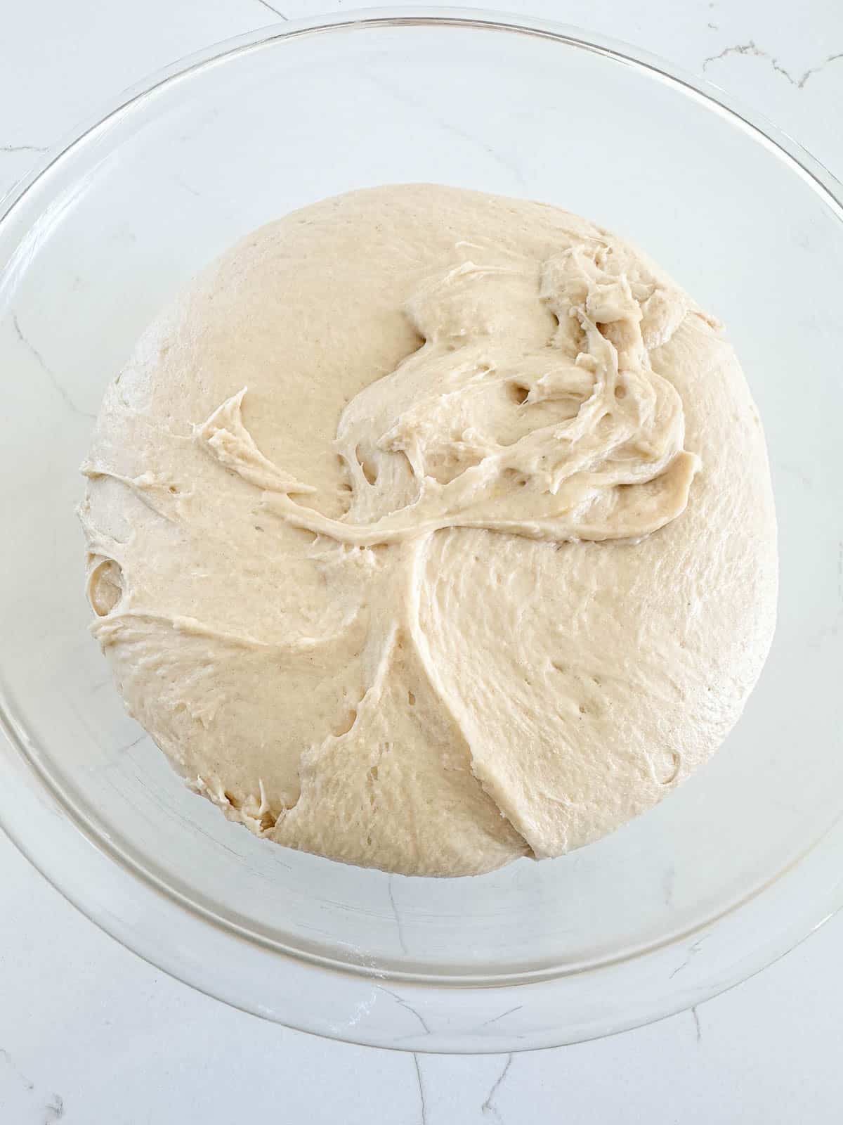 A ball of raw sourdough rising in a clear glass bowl.