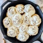 Sourdough cinnamon rolls topped with white frosting in a cast iron skillet.