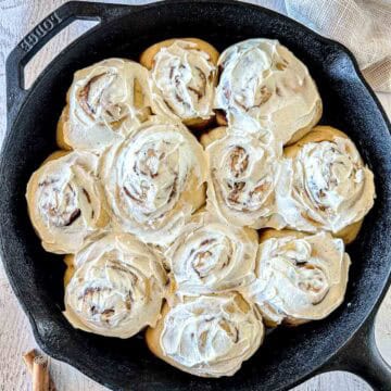 Sourdough cinnamon rolls topped with white frosting in a cast iron skillet.