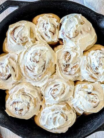 Sourdough cinnamon rolls topped with white frosting in a cast iron skillet.